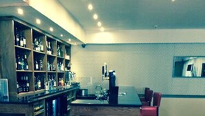 Zona de bar con estantes de botellas, una máquina de café y un área de estar con sillas.