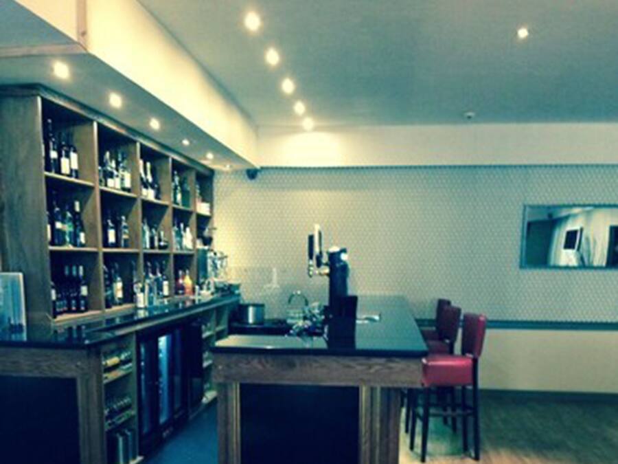 Zona de bar con estantes de botellas, una máquina de café y un área de estar con sillas.