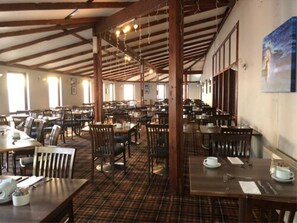 A large dining hall with high ceilings and wooden beams, featuring multiple tables and chairs arranged for dining. - King Robert Hotel (Stirling)