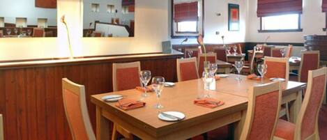 A restaurant with wooden tables and red chairs, some with wine glasses and cutlery.
