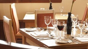 Una mesa de comedor preparada con platos, cubiertos y copas de vino, con una silla de madera y un jarrón sobre la mesa.