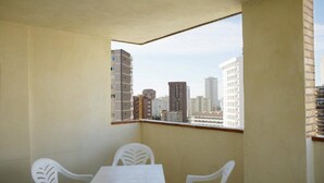 A balcony with a table and chairs, a view of city buildings, and a window with a wooden frame. - Benimar (Benidorm)