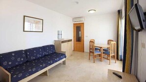 A small, simple room with a sofa, a table, chairs, a TV, and a door. - Benimar (Benidorm)