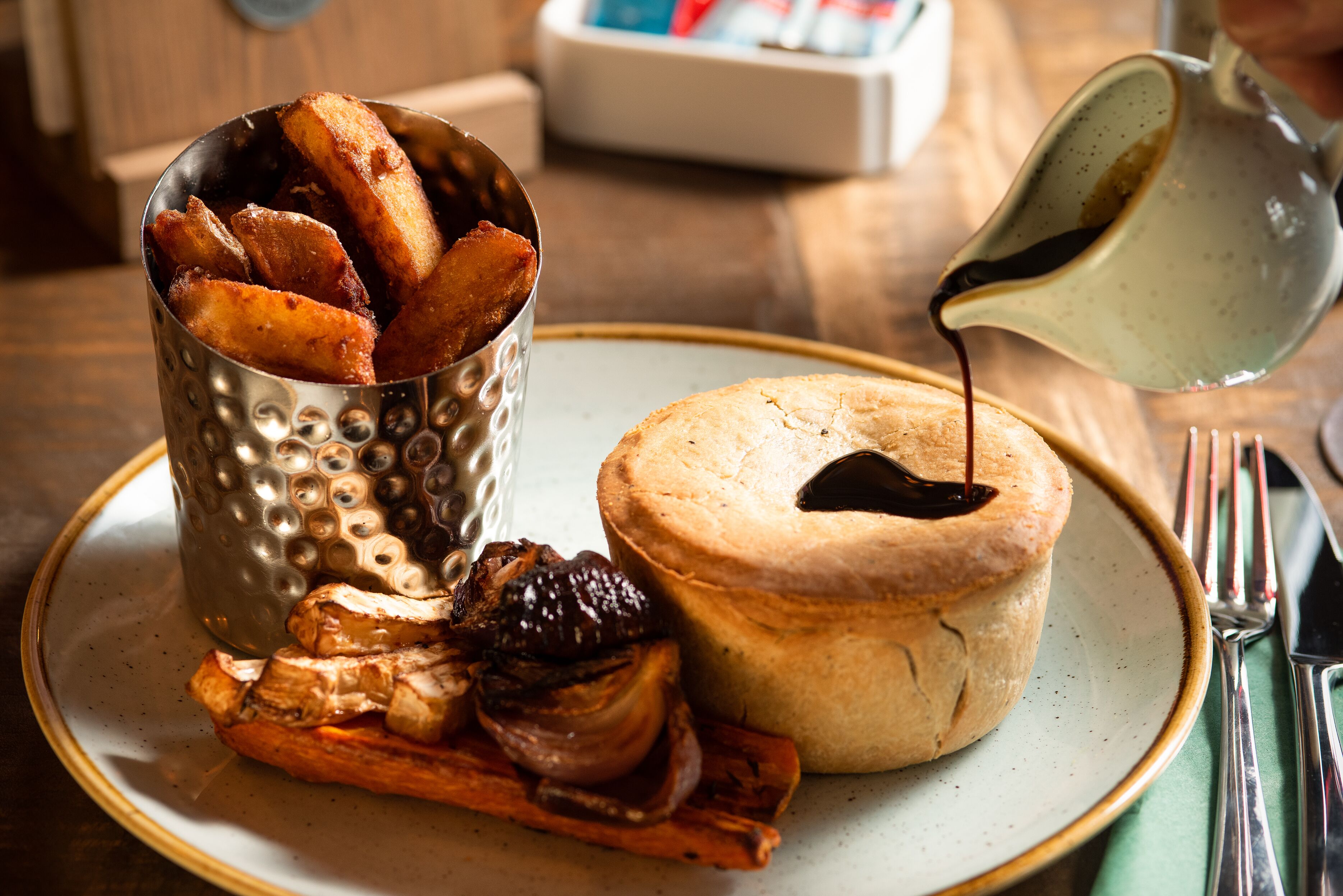 A plate with a baked pastry, a metal container of fried potatoes, and a small bowl of sauce.