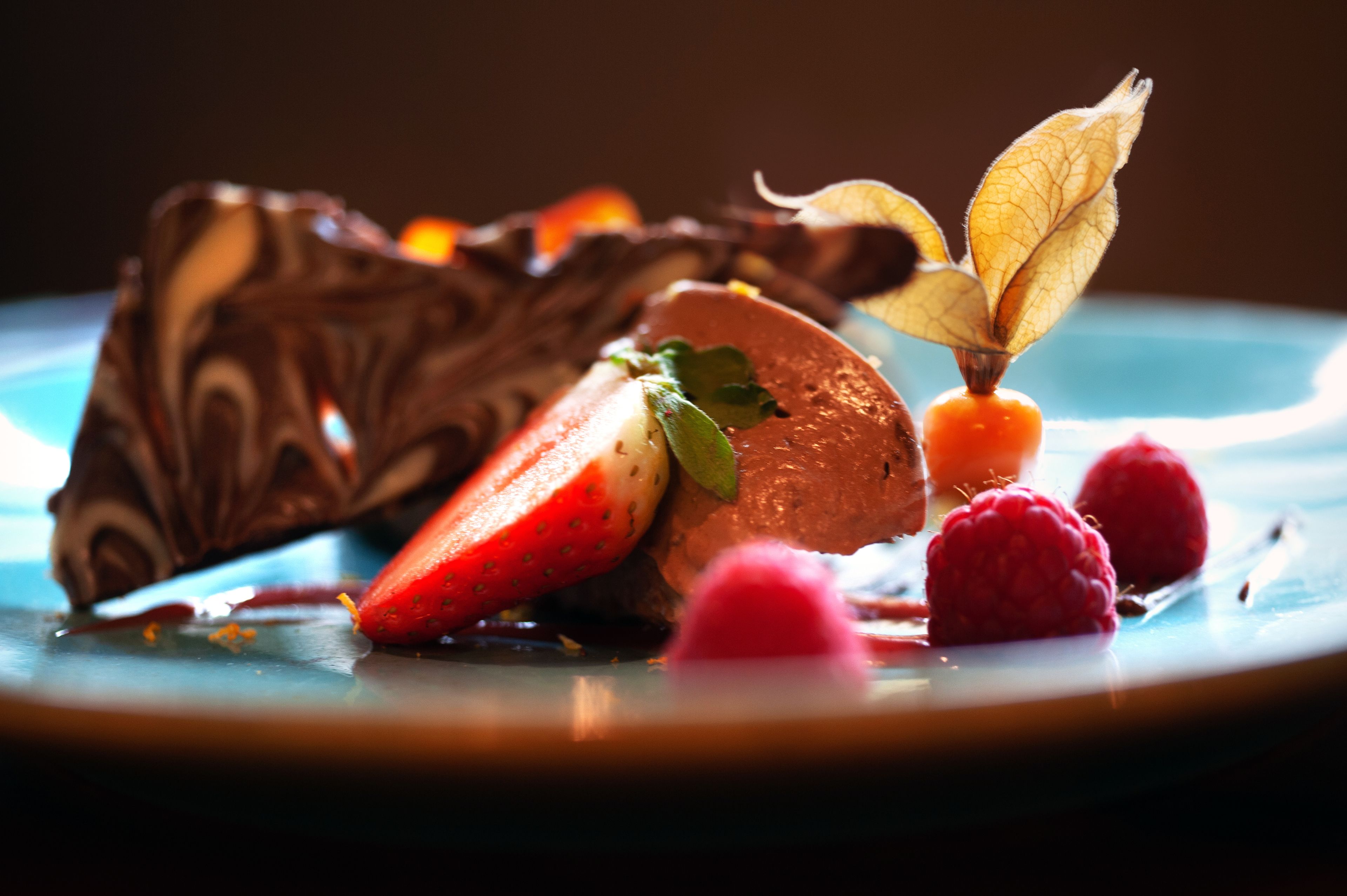 A dessert plate with chocolate, strawberries, raspberries, and a decorative leaf.