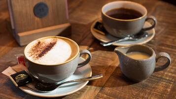 Two cups of coffee on saucers with spoons, a small pitcher, and a wooden box on a wooden table.