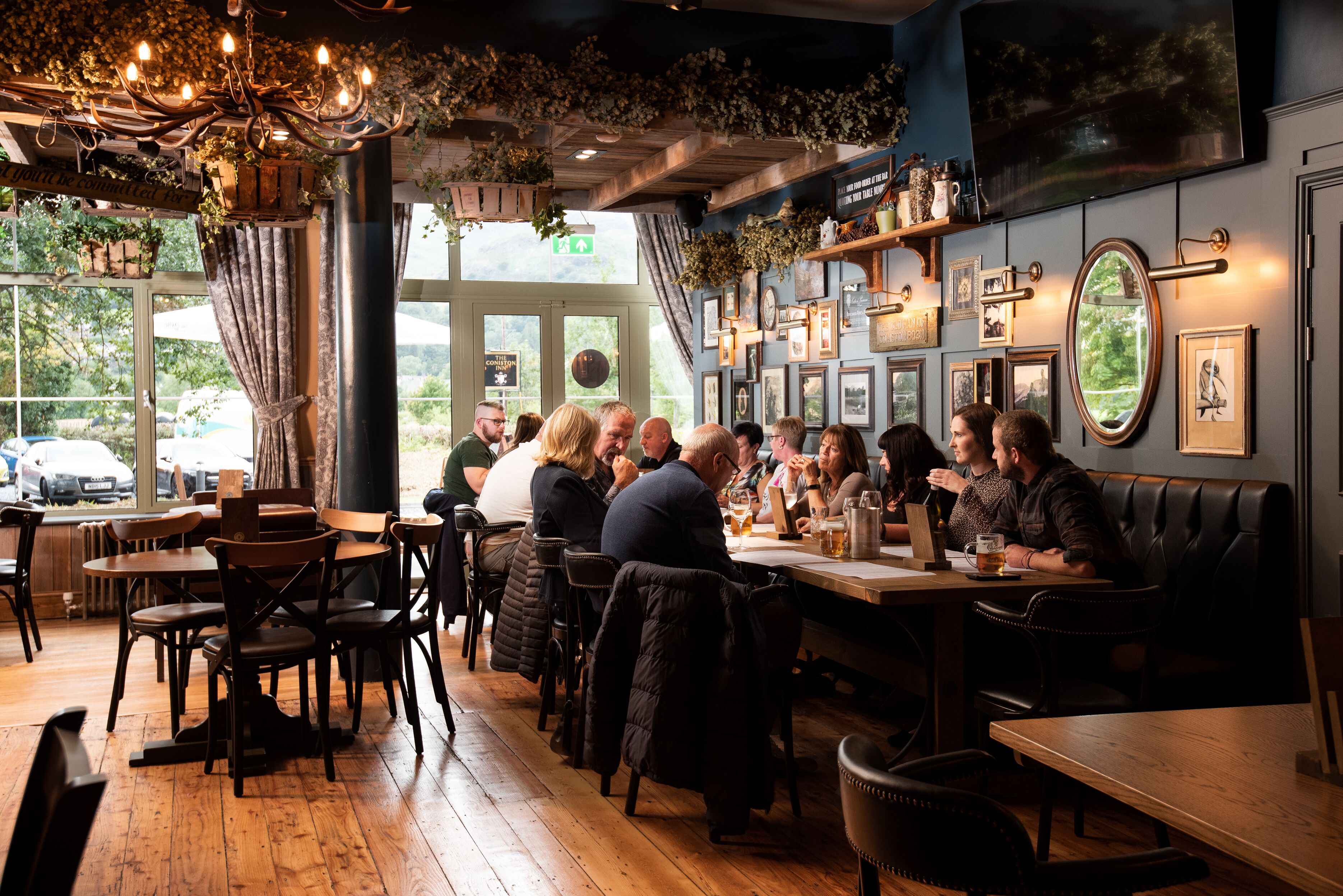 A restaurant with wooden tables and chairs, a chandelier, and framed pictures on the walls.
