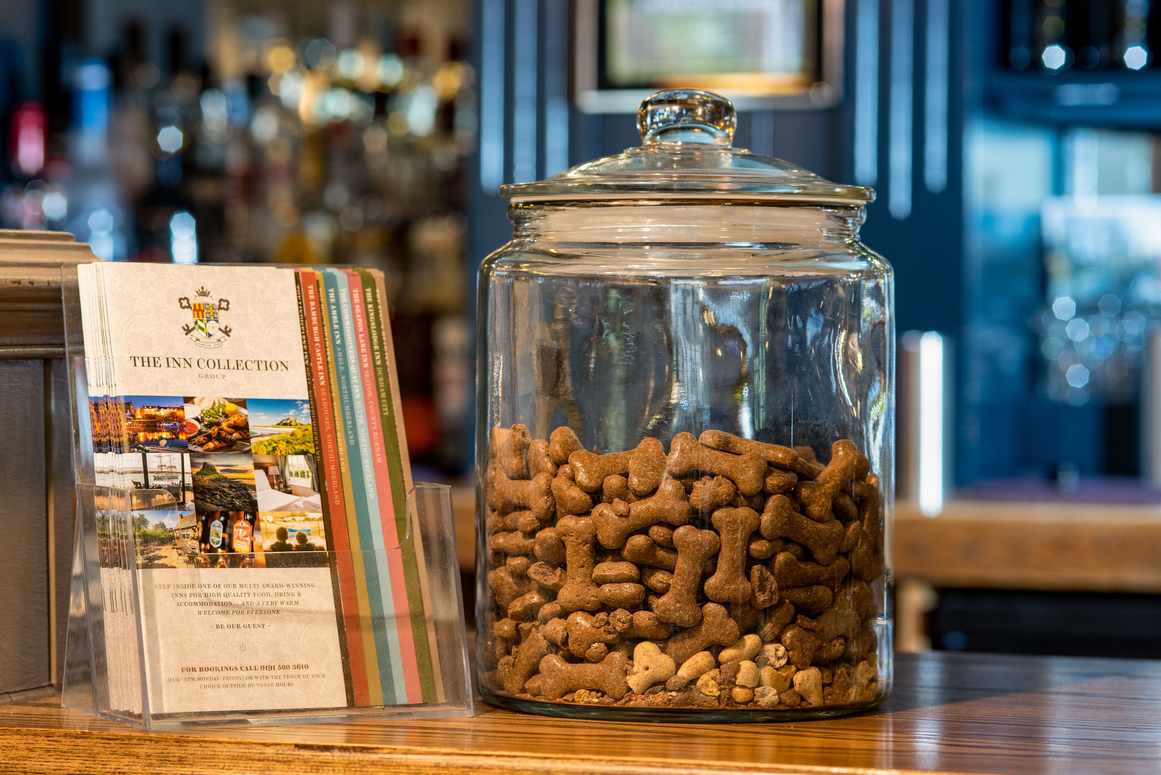 A glass jar filled with dog treats on a wooden table, next to a brochure titled "The Inn Collection Group".