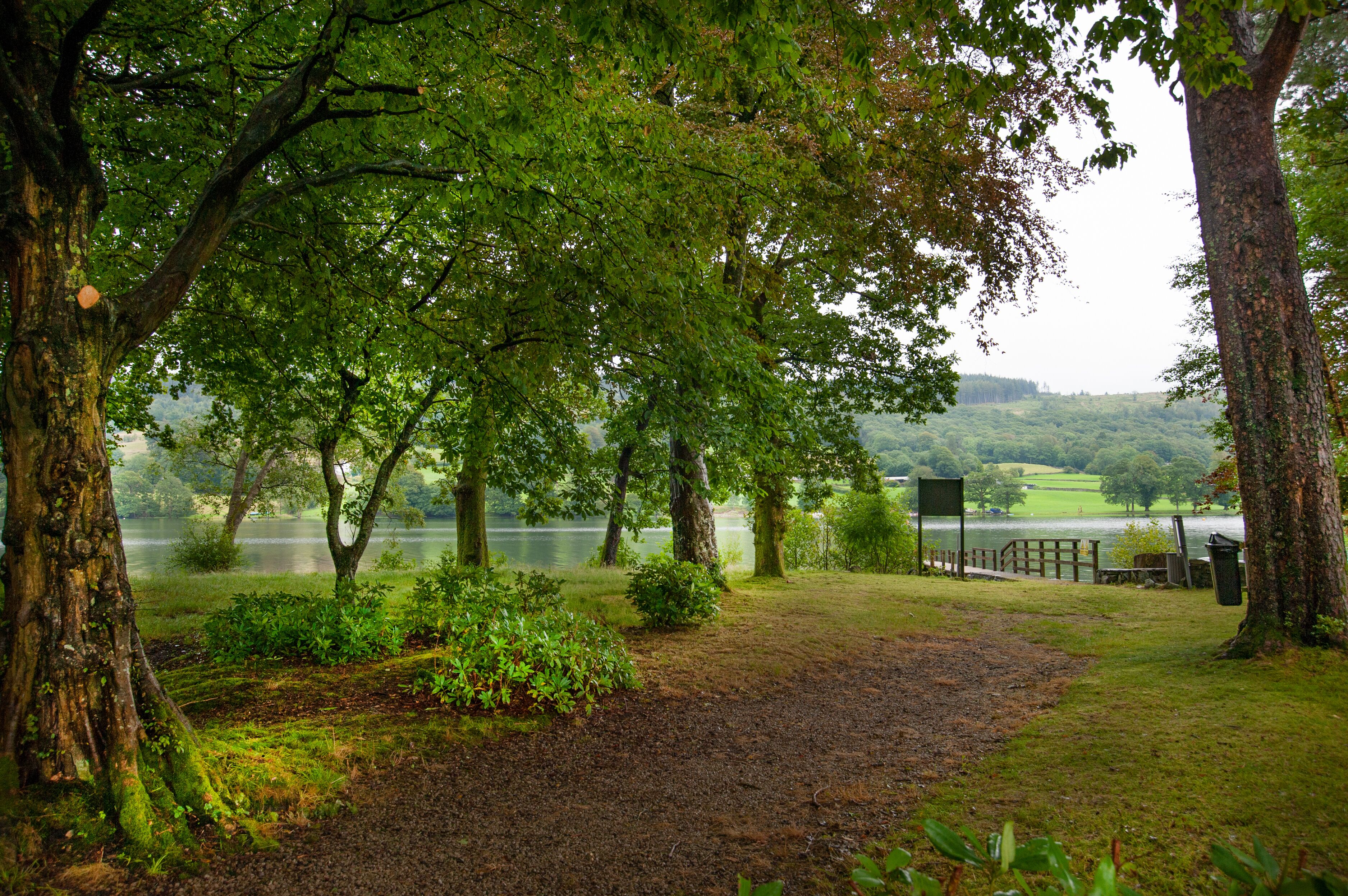 A park with a gravel path, trees, and a lake in the background.