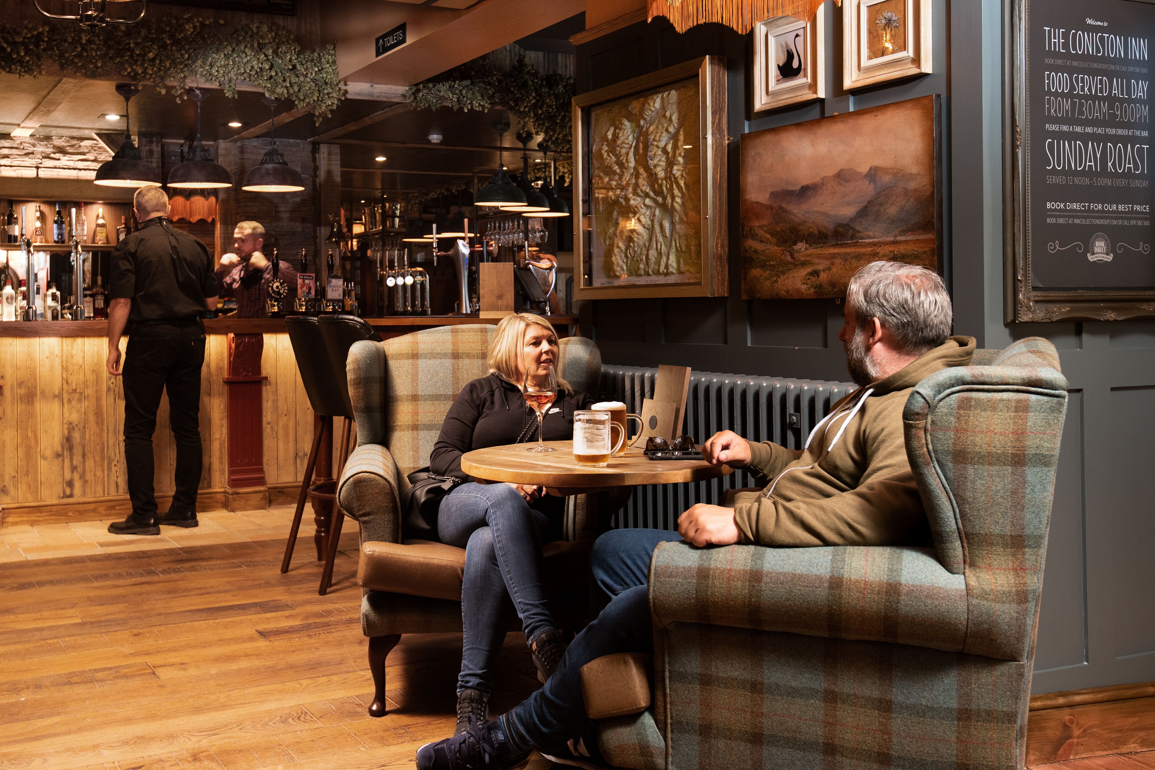 A cozy bar area with wooden floors, a bar counter, and seating with a checkered pattern.