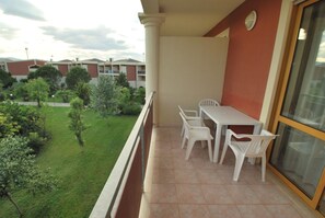 A balcony with a table and chairs, overlooking a green lawn and buildings in the background. - Akiris (Nova Siri)