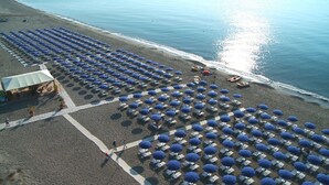 An aerial view of a beach with rows of umbrellas and chairs, a small building, and the ocean in the background. - Akiris (Nova Siri)