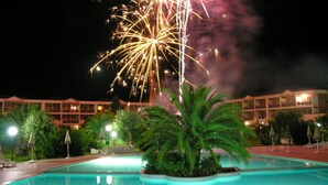 A hotel pool with a palm tree and a building in the background. - Akiris (Nova Siri)
