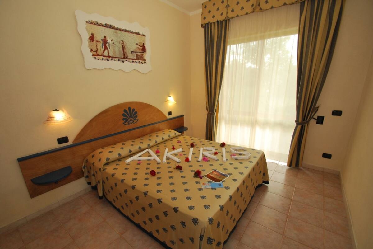 Un dormitorio con cama, cabecera, un cuadro en la pared y cortinas.