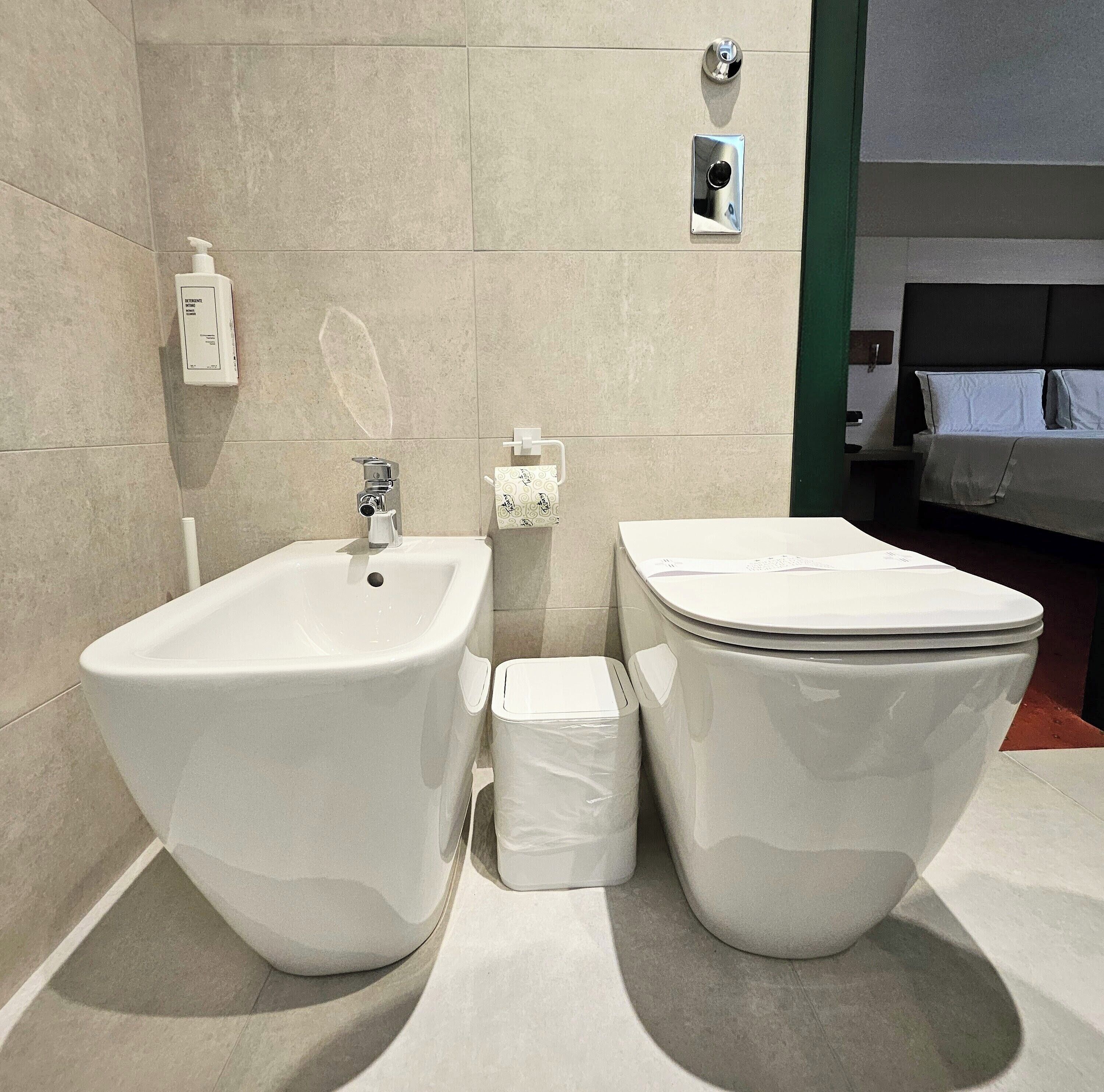 A modern bathroom with a bidet, toilet, and a small trash bin.