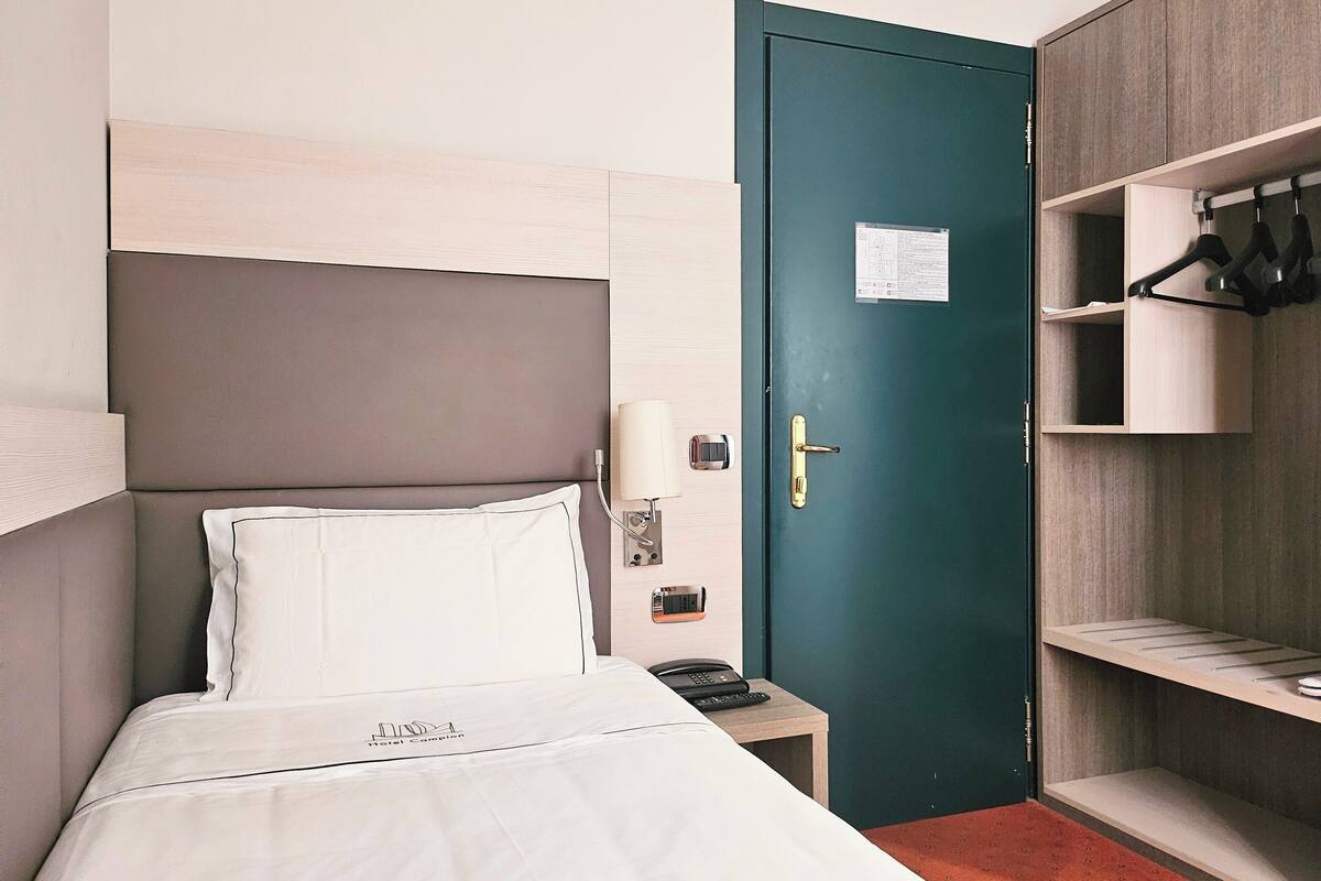 A hotel room with a bed, a desk with a phone, a door with a keycard slot, and a wardrobe with hangers.