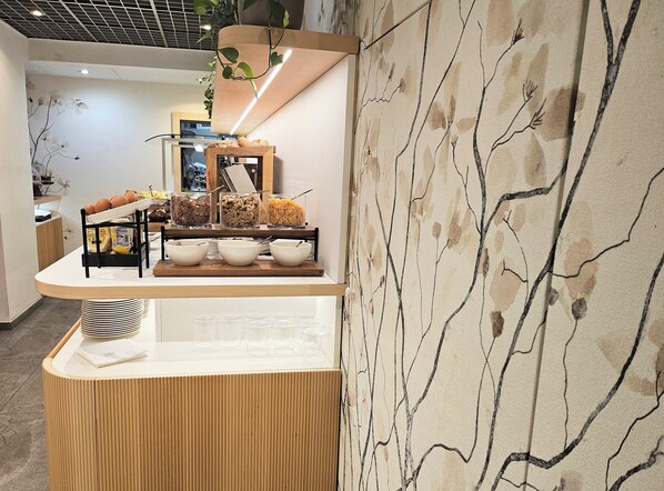 A breakfast bar with bowls of cereal and fruits, a coffee machine, and a plant. - Hotel Campion CityLife (Milan)