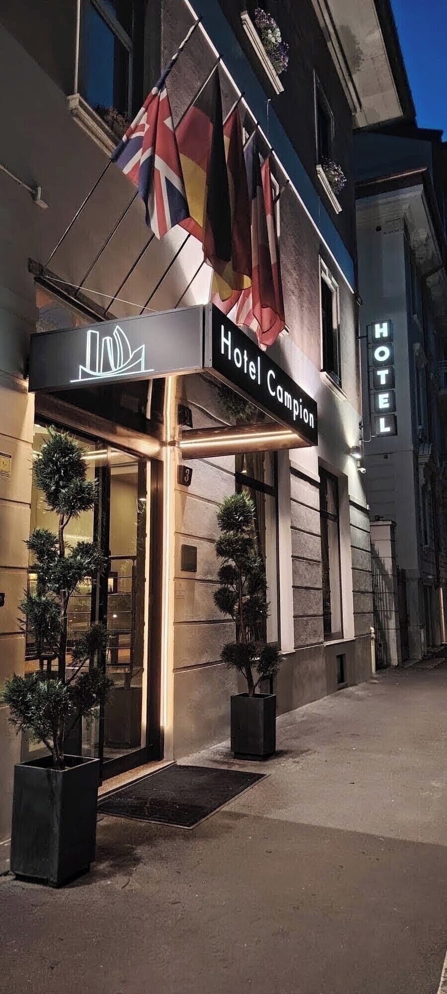 Entrada de un hotel con un cartel que dice 'Hotel Campion' y un letrero de neón encima.