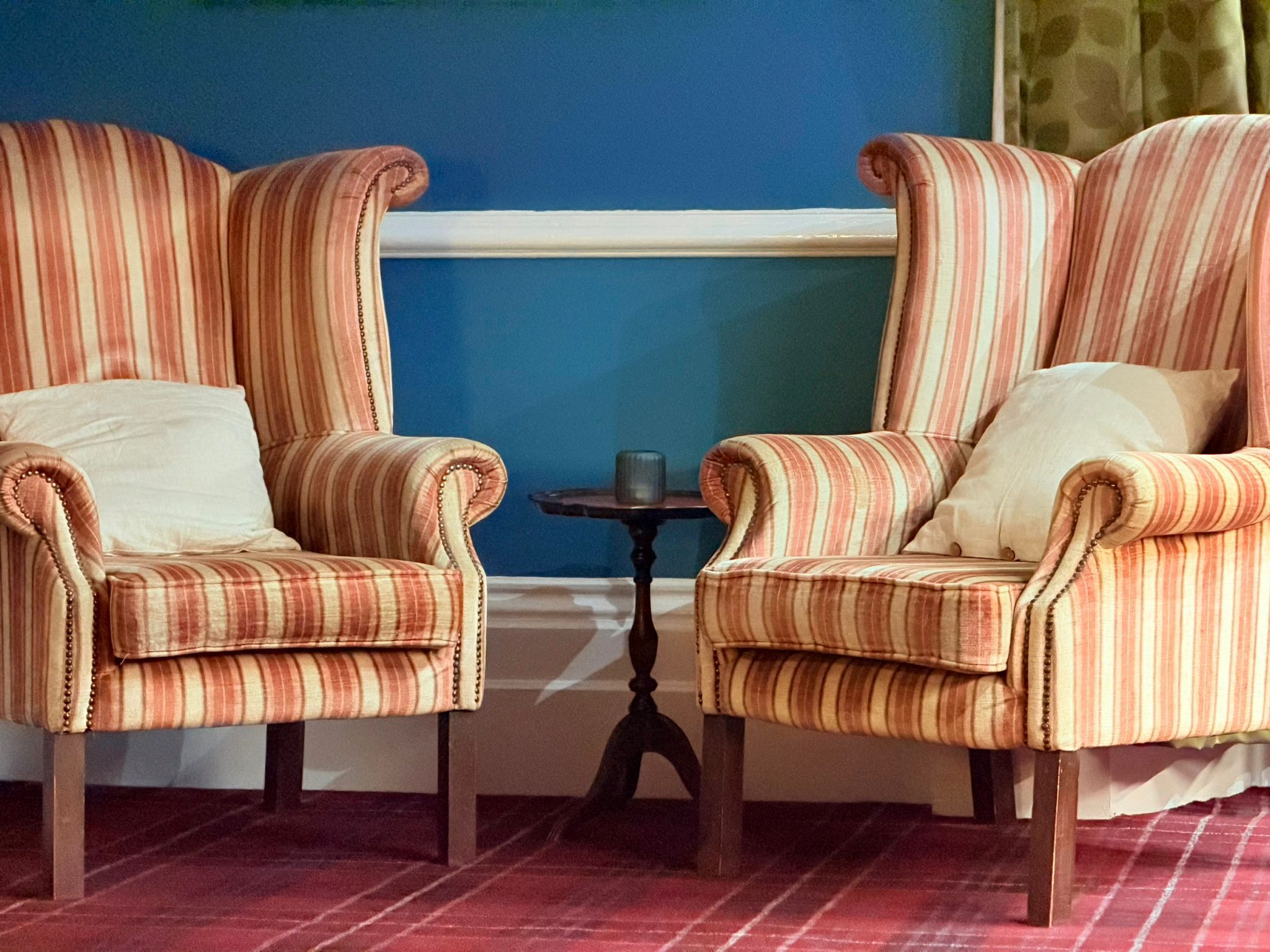 Two striped armchairs with cushions, a small round table, and a window with a blue wall behind them.