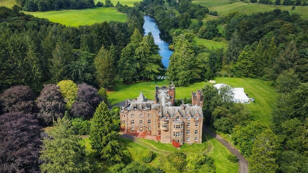 Um edifício grande e histórico rodeado por vegetação exuberante e um rio.
