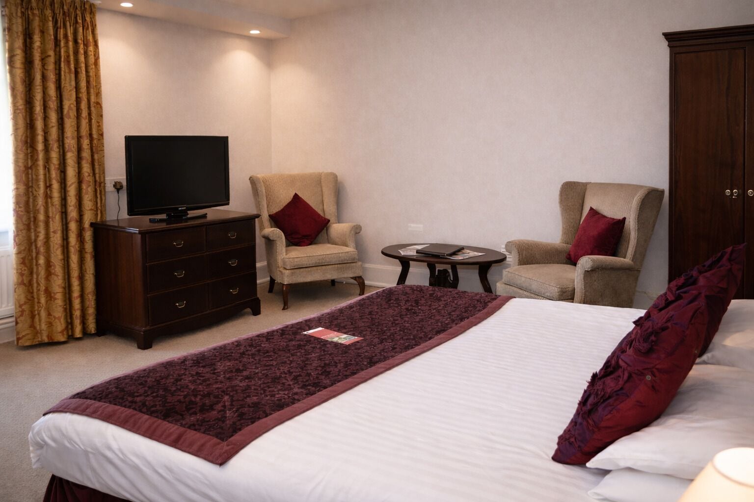 Een hotelkamer met een groot bed, twee fauteuils, een tafeltje, een televisie en een kledingkast.
