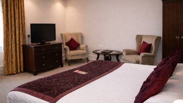 A hotel room with a large bed, two armchairs, a small table, a TV, and a wardrobe.