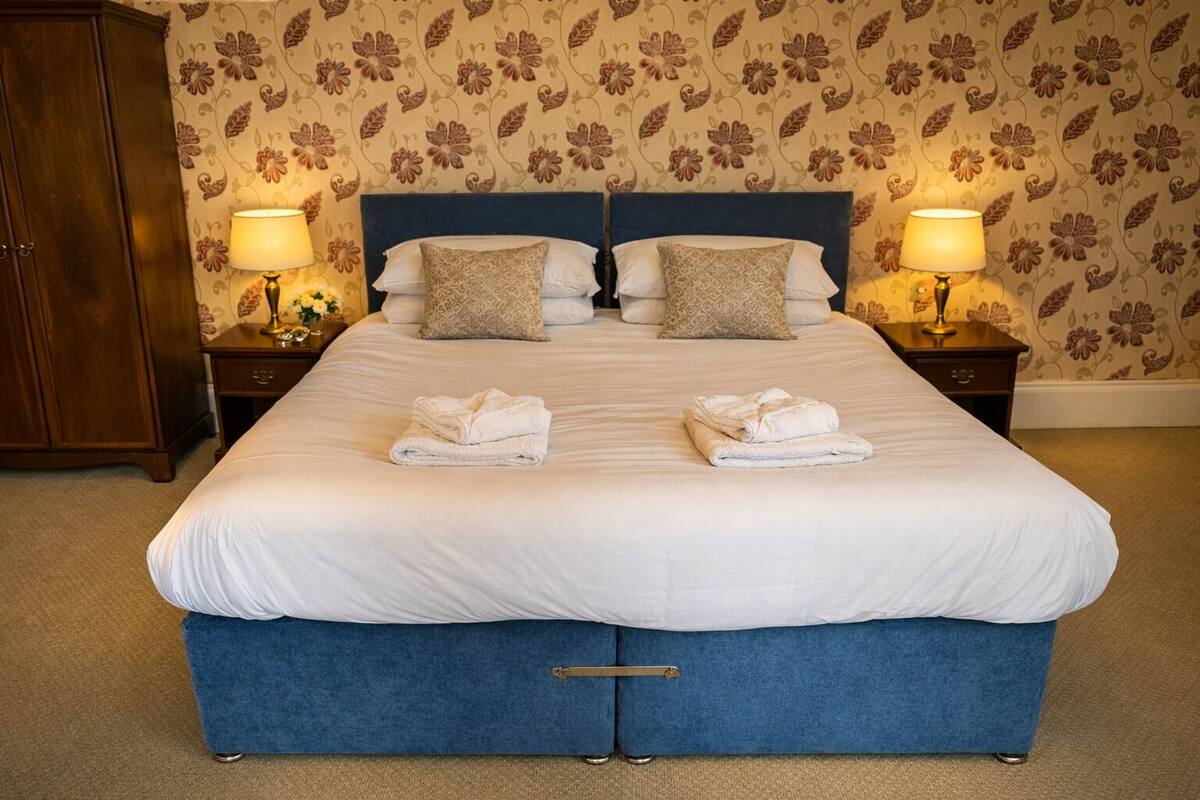 A neatly made bed with two pillows, a blue upholstered headboard, and two bedside lamps.