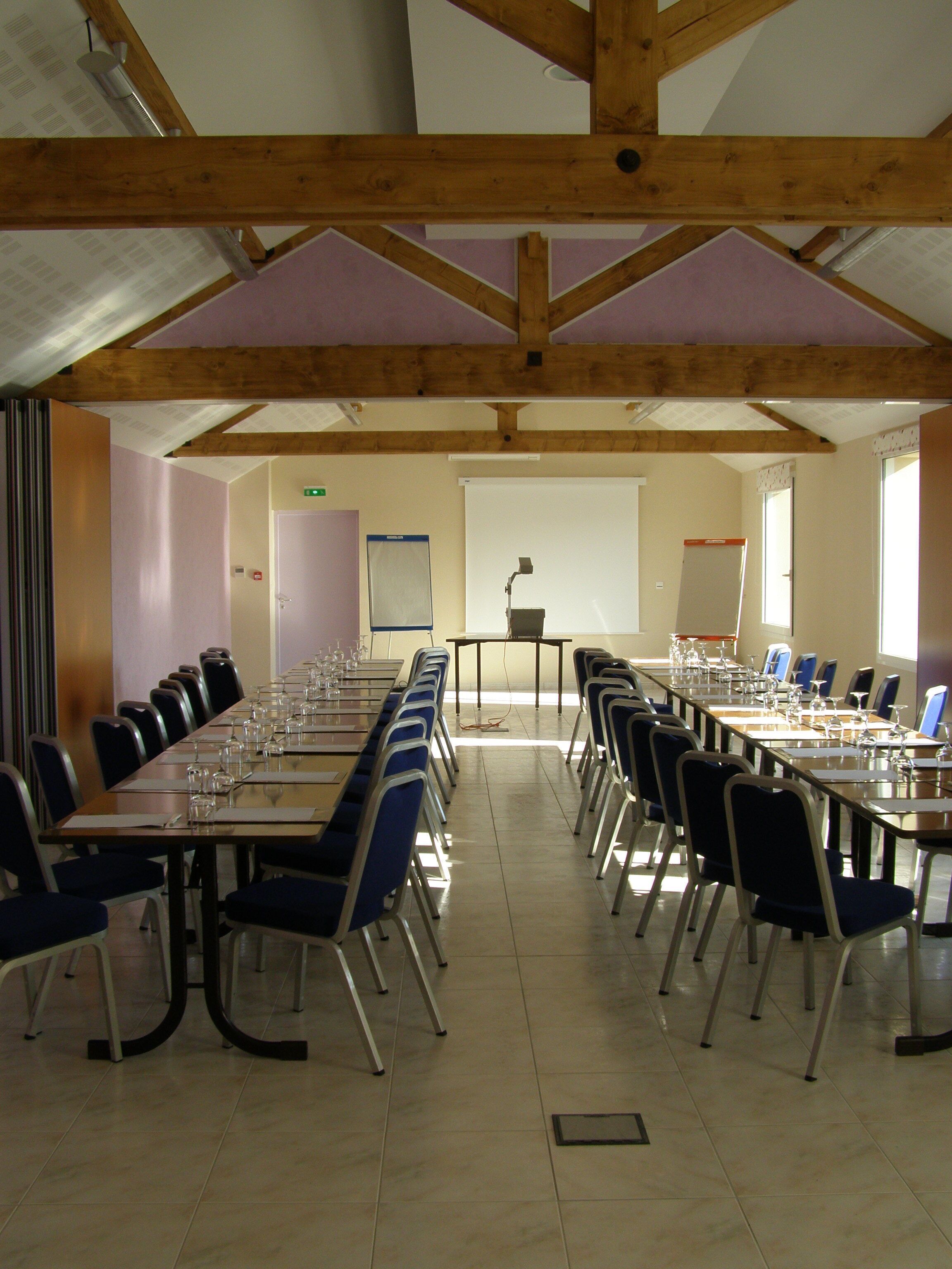 A conference room with long tables and chairs, a projector screen, and a stage with a podium.