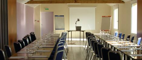 A conference room with long tables and chairs, a projector screen, and a stage with a podium.