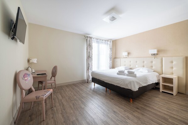 A hotel room with a bed, a desk, a chair, a TV, and a window with curtains.