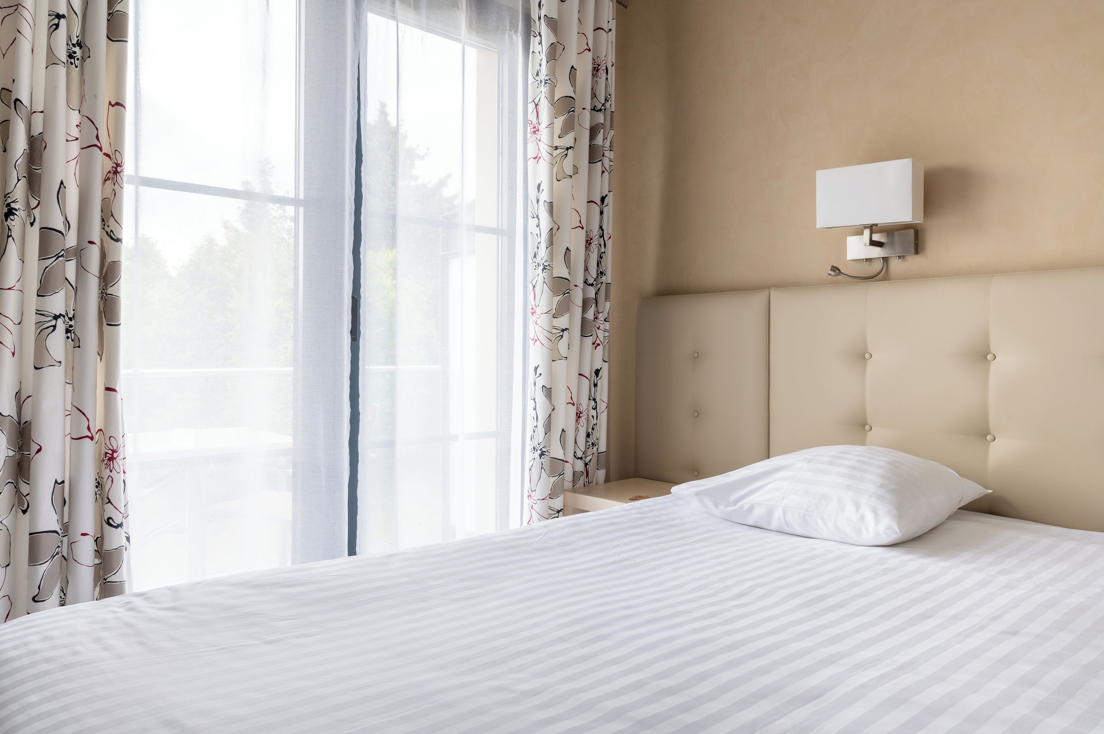 Une chambre d’hôtel avec un grand lit, une table de chevet, une lampe fixée au mur et une fenêtre avec des rideaux.