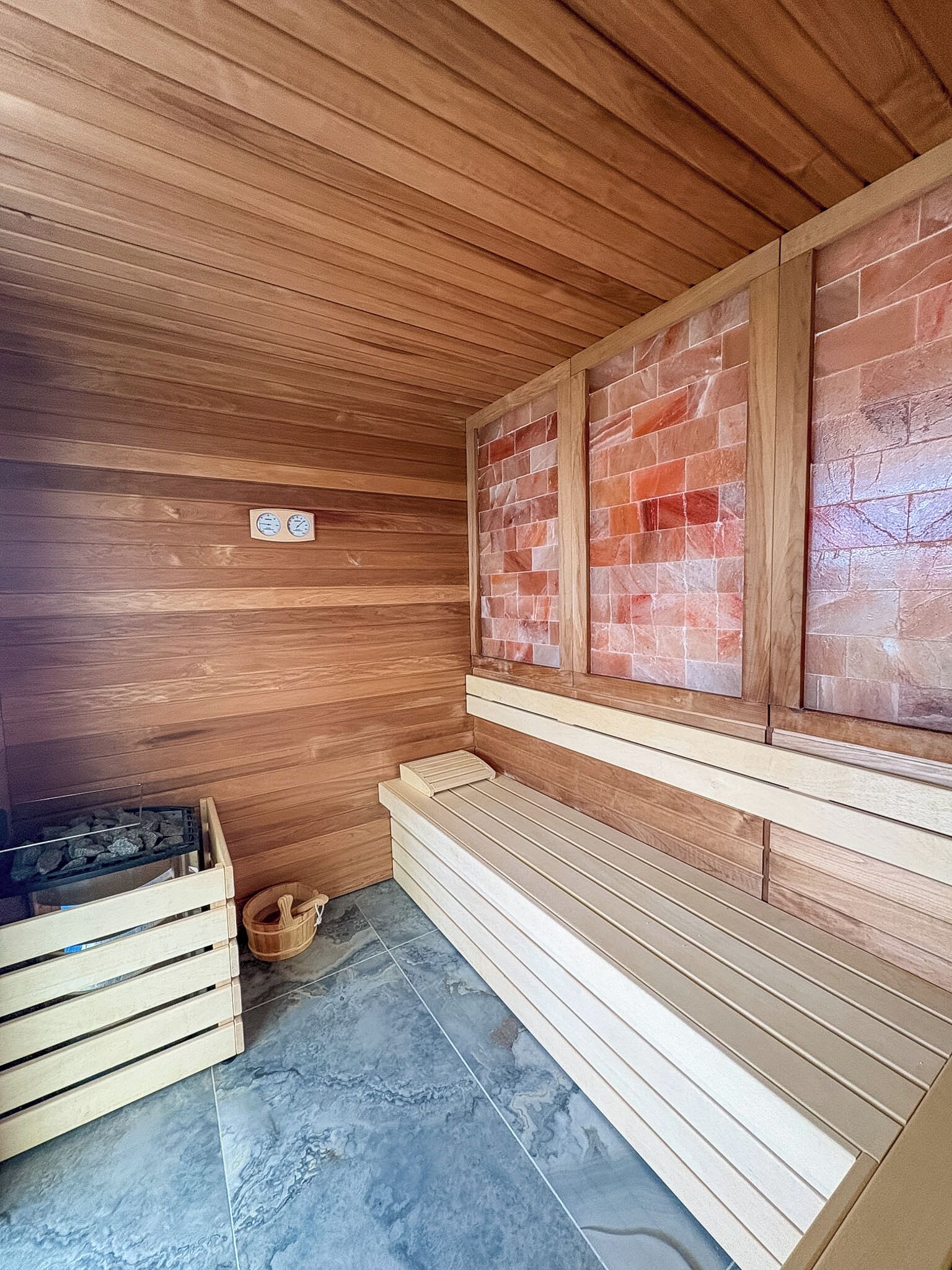 A sauna with wooden benches, a tiled floor, and a brick wall.