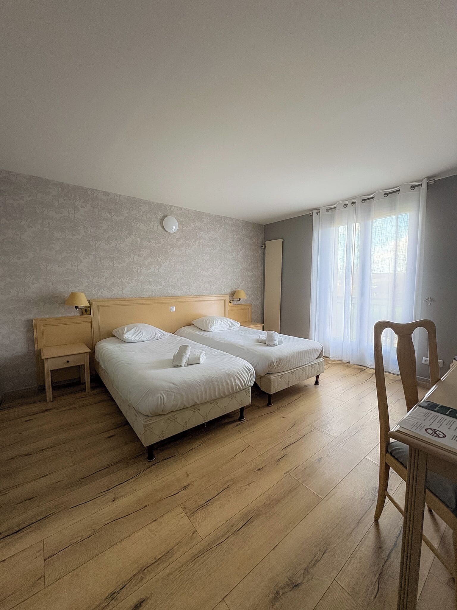 A hotel room with two beds, a wooden floor, a small table, and a chair.