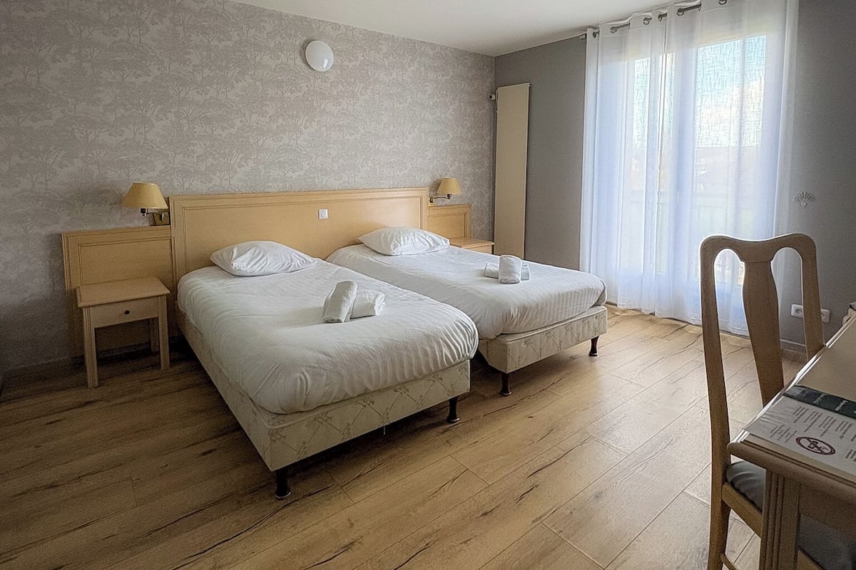 A hotel room with two beds, a wooden floor, a small table, and a chair.