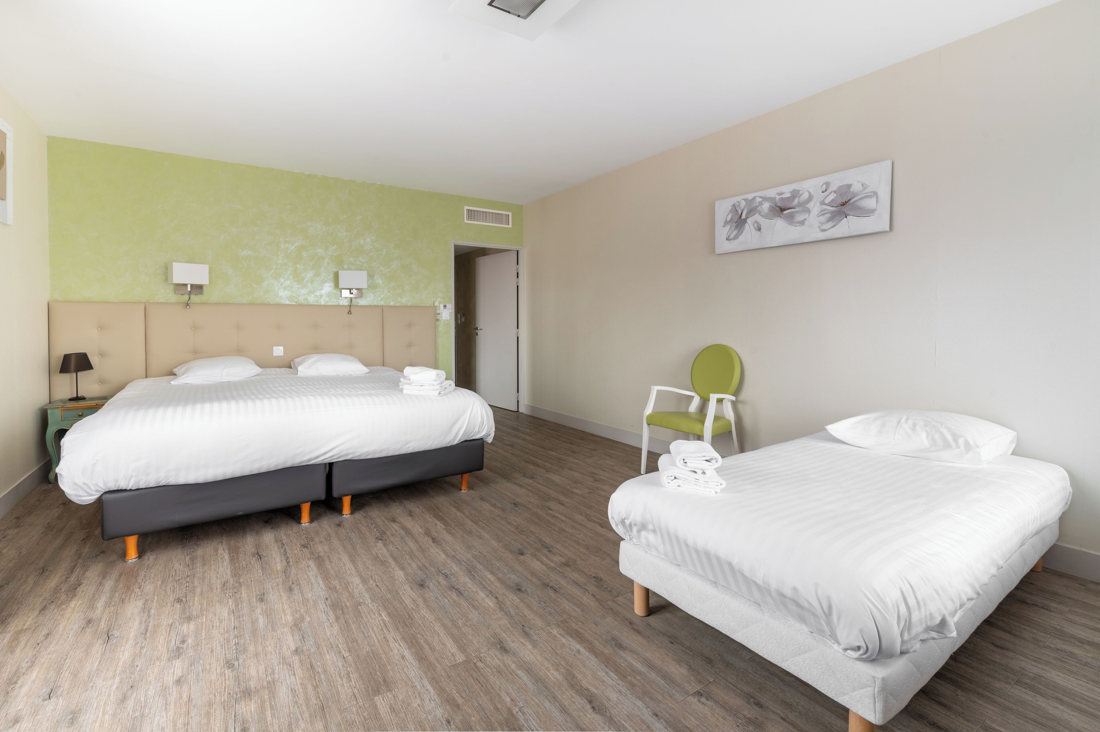 A hotel room with two beds, a green wall, a painting, and a chair.
