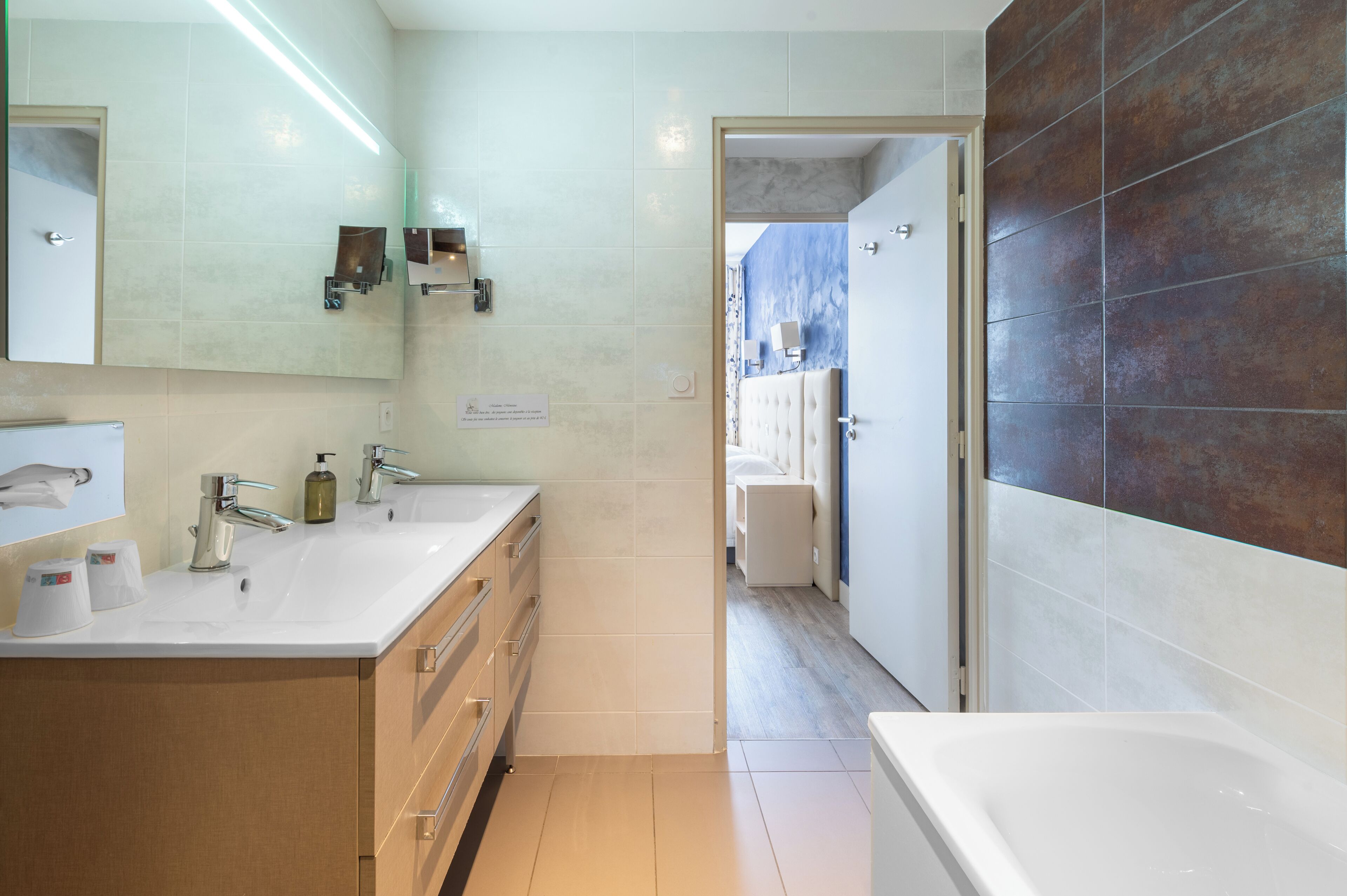 A modern bathroom with a double sink, a large mirror, and a bathtub.