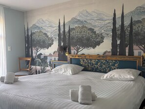 Een hotelkamer met een groot bed, een hoofdeinde met bloemenmotieven, een muurschildering van een landschap en een stoel bij het raam.