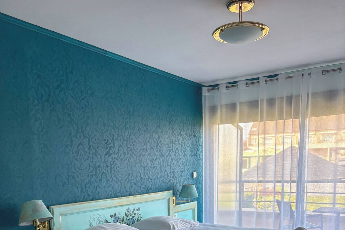 Een slaapkamer met een groot bed, twee nachtkastjes, een raam met gordijnen en een plafondlamp.