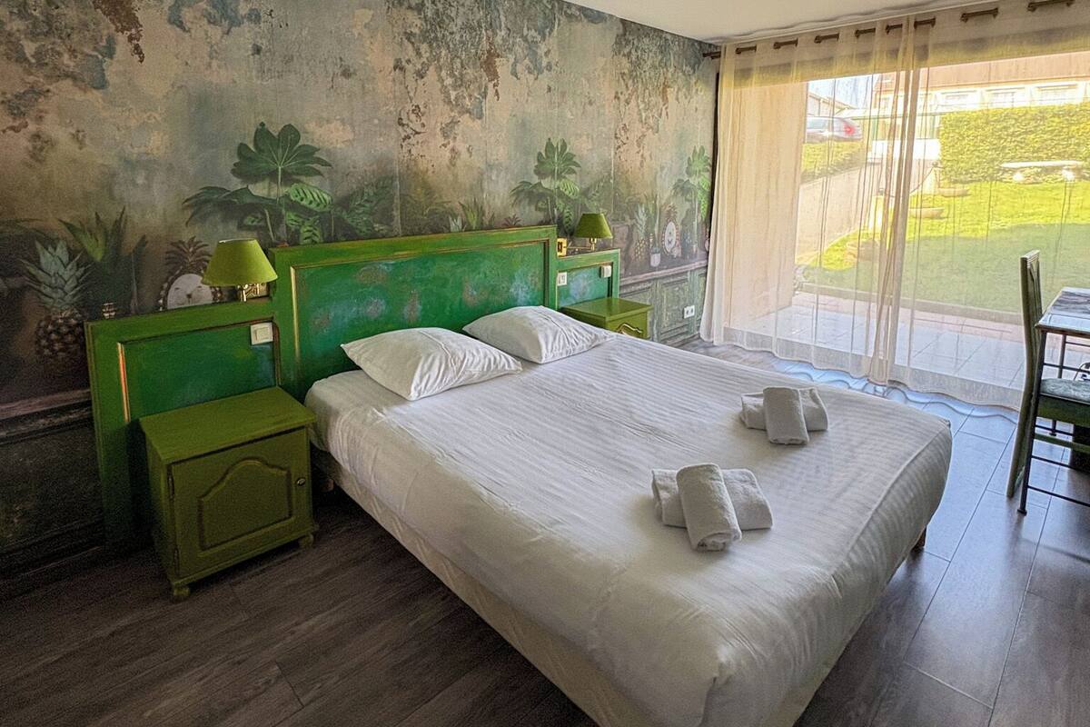 Een slaapkamer met een groot bed, groene nachtkastjes, een groen hoofdeinde en uitzicht op een tuin door een schuifdeur.
