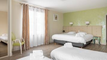 Une chambre d’hôtel avec deux lits, un fauteuil vert, une petite table et un miroir.