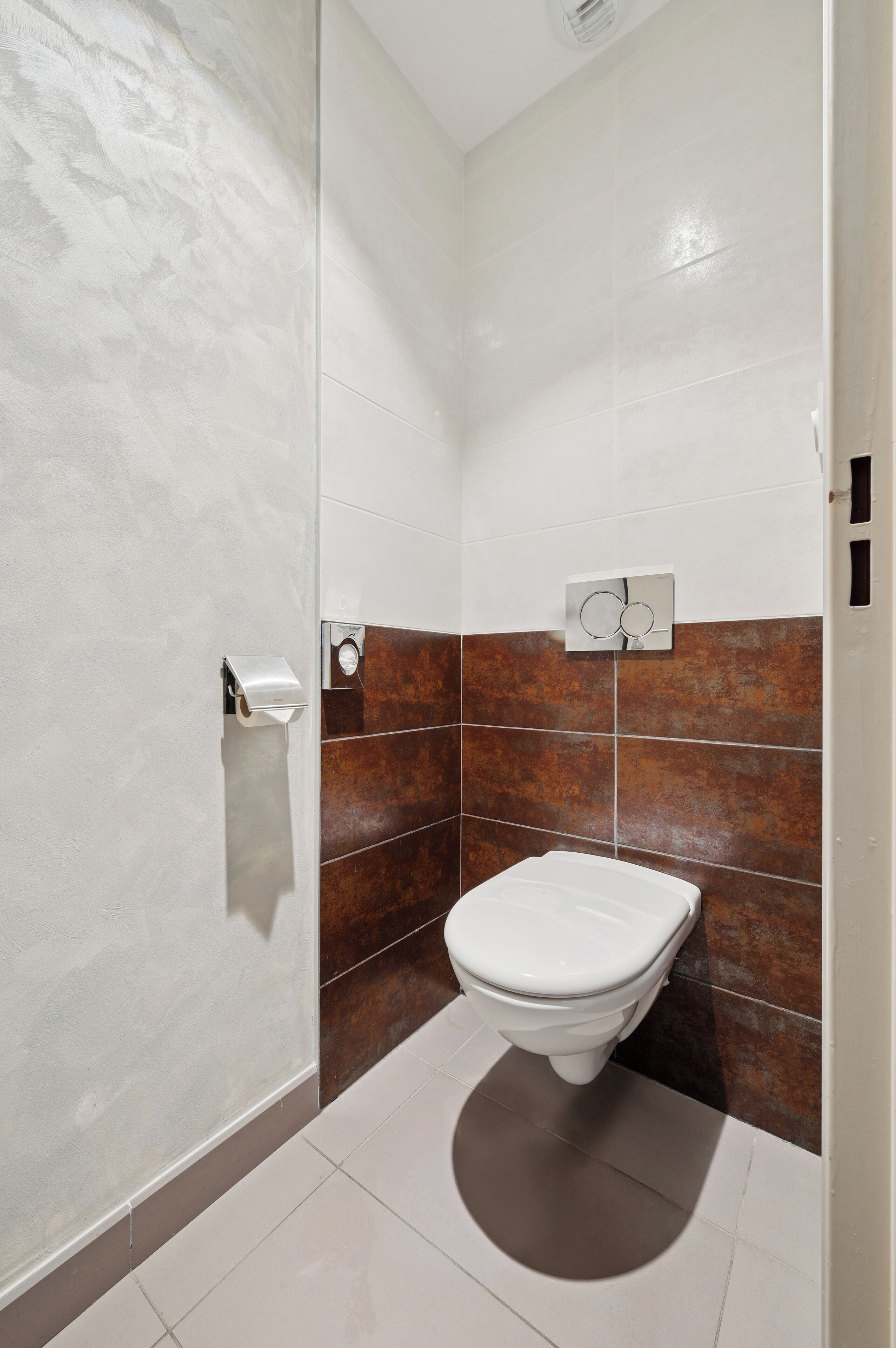 A bathroom with a toilet, a hand dryer, and a towel dispenser.
