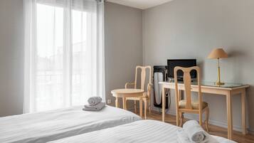 Een hotelkamer met twee bedden, een bureau met een computer, een stoel en een lamp.