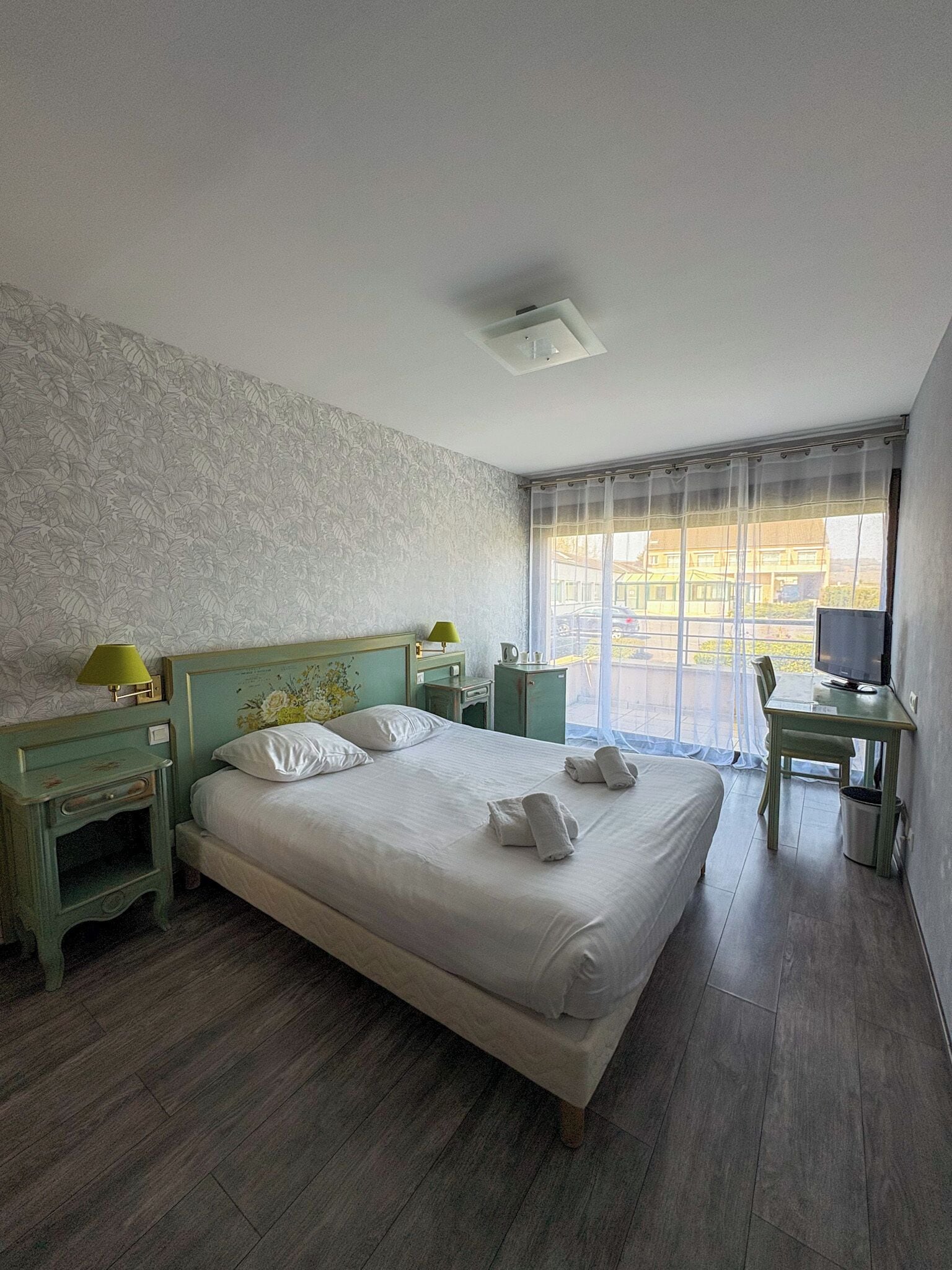 Un dormitorio con cama, escritorio, silla, lámpara y televisor.