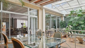 Un comedor espacioso con una mesa y sillas de vidrio, rodeado de amplias ventanas y vistas a un jardín exuberante.