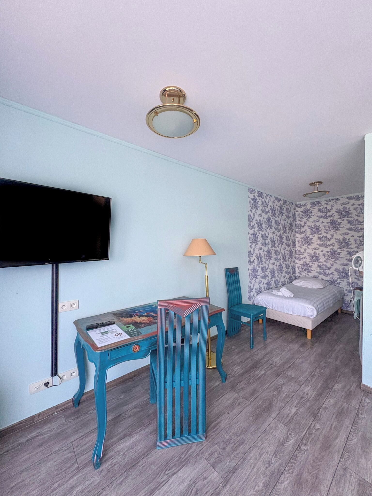 Una habitación con una cama, televisión, mesa con lámpara y una silla.