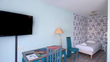 Una habitación con una cama, televisión, mesa con lámpara y una silla.
