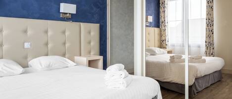 A modern hotel room with a large bed, a nightstand, a wall-mounted lamp, and a large mirror.