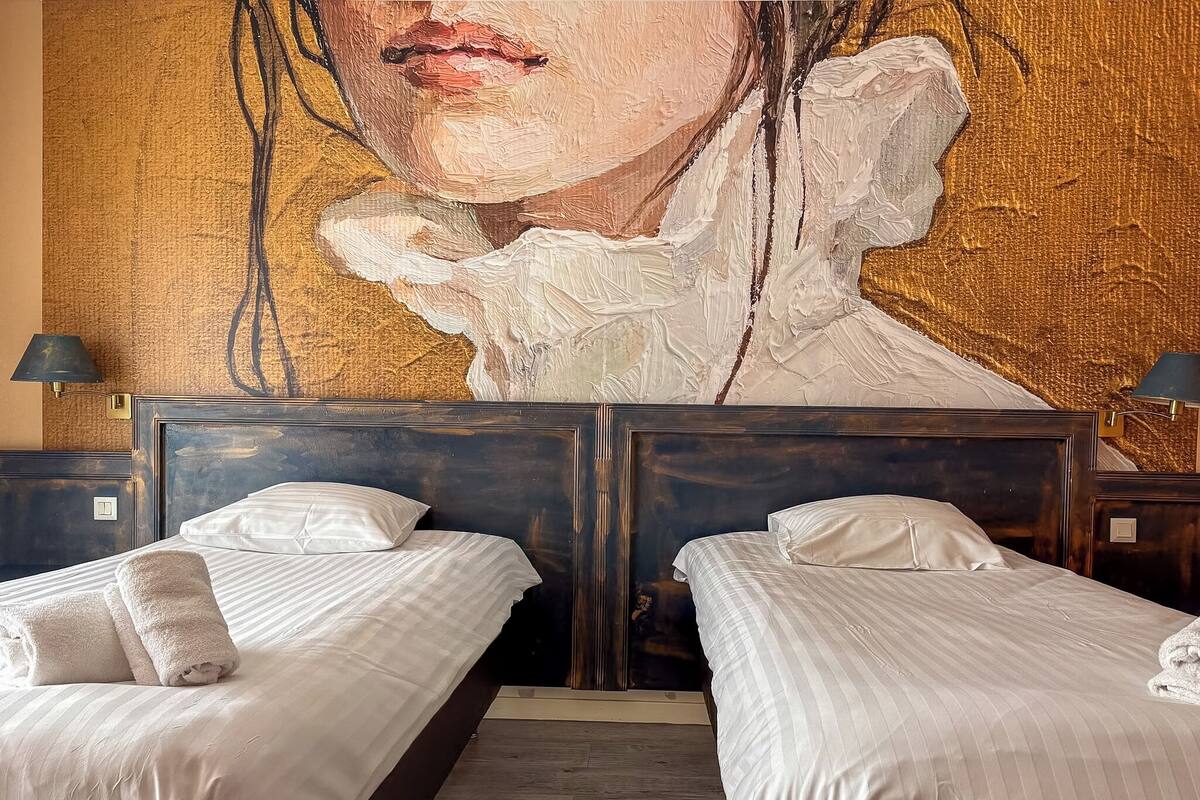 Een hotelkamer met twee bedden, een groot muurdecor en een houten vloer.