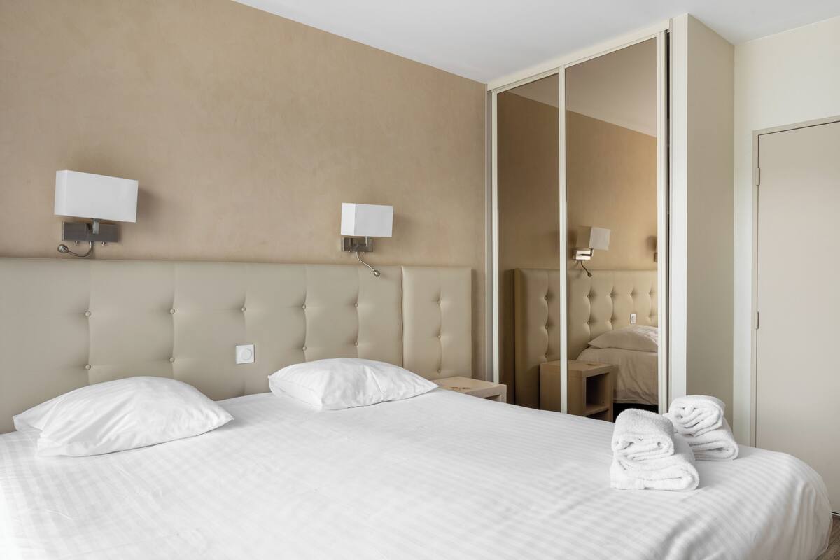 Een hotelkamer met een groot bed, twee wandlampen, een spiegel en een garderobe.