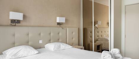 Une chambre d’hôtel avec un grand lit, deux lampes fixées au mur, un miroir et une armoire.